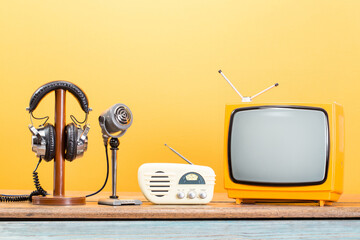 Retro TV, radio, old microphone and headphones front yellow background. Vintage style filtered photo