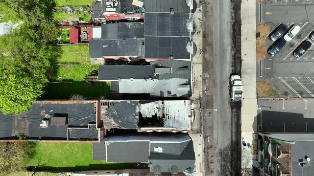 Aerial top down of destroyed old houses in dangerous american town during sunny day. Roadworker improving road. Narrow homes in suburb district.  Low income housing in Pennsylvania. Flyover shot.