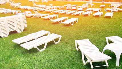 A large grassy field with many white lawn chairs scattered throughout. The chairs are arranged in rows and are empty. The scene gives off a peaceful and relaxing vibe