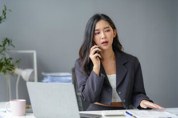 Focused young asian businesswoman in modern office multitasking on laptop and phone call, feeling pressure of looming deadline