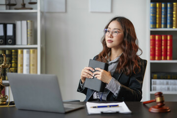 Focused asian lawyer in office, with law book, gavel, scales, and laptop, contemplating legal...