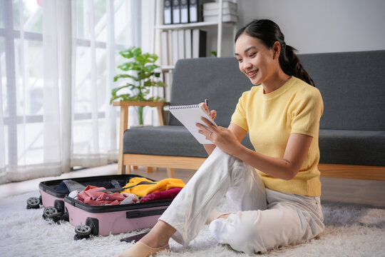 Excited woman sits on floor, planning trip with open suitcase and notebook. Organized packing list for upcoming adventure - Powered by Adobe