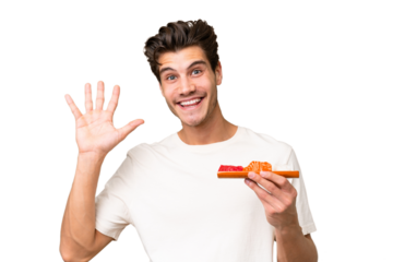 Young caucasian man holding sashimi over isolated background saluting with hand with happy expression