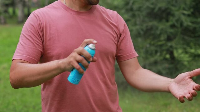 Close-up of a man spraying protective repellent on his skin while walking in the park