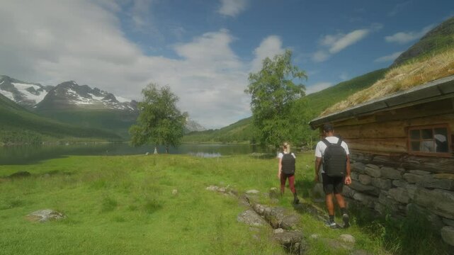 A young couple hiking near a rustic cabin in scenic Innerdalen, Norway on a sunny day