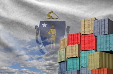 Massachusetts US state flag and big stack of shipping cargo containers in docks with sky background...