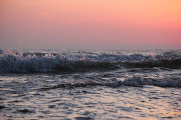 Dark sea waves near the coast against the backdrop of a bright pink sunset sky