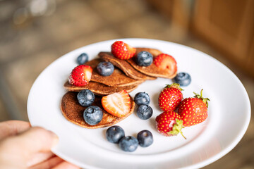 A man's hand holds a plate of sugar-free, gluten-free green buckwheat fritters with strawberries...