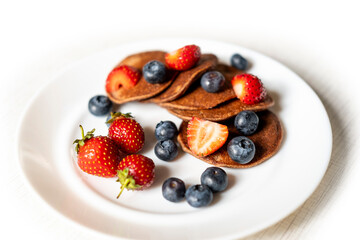 In a plate of green buckwheat flour pancakes. Strawberries and blueberries. Useful and tasty dessert prepared with your own hands.