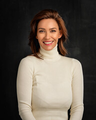 Obraz premium Studio portrait of a brunette haired woman wearing turtleneck sweater and cheerful smiling against isolated black background. Copy space.