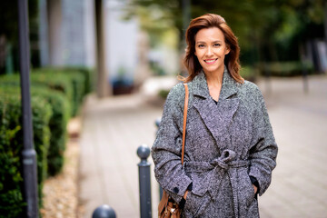 Mid aged woman with brunette hair walking outdoor in the city street on autumn day