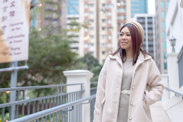 Thirty-something Hong Kong woman with reddish-brown hair walking by a large fountain in Kowloon Park, Tsim Sha Tsui, Kowloon Island, Hong Kong, during a cold winter.