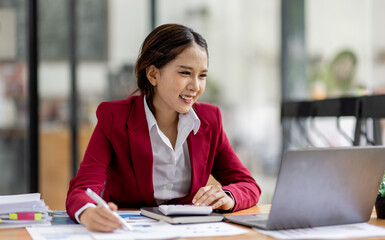 Business asian woman working on laptop, using financial calculator at modern office, analyzing business document with financial graph, market report on digital tablet, business data analysis concept