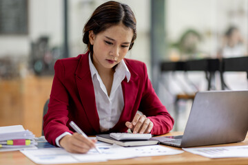 Business asian woman working on laptop, using financial calculator at modern office, analyzing business document with financial graph, market report on digital tablet, business data analysis concept