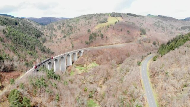 Aerial: train going uphill and crossing a viaduct in the french Massif Central