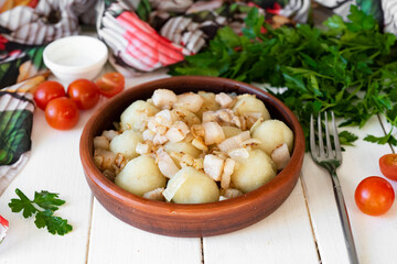 Dumplings with onions and bacon on a brown plate on a white background. Lunch for the whole family. Homemade potato dumplings. Close-up