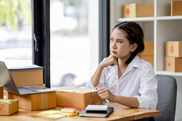 Asian woman think hard serious working of sme laptop computer at home selling online start up small business owner, e-commerce ideas concept.