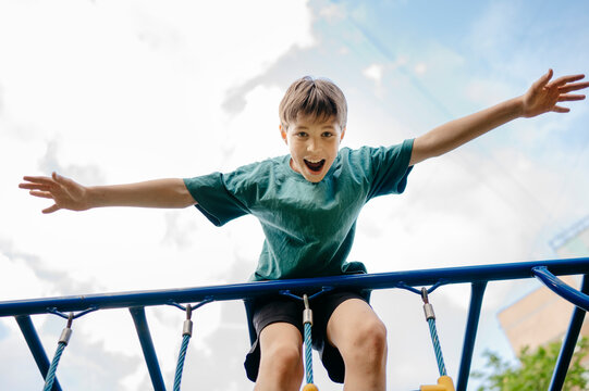 Boy with arms outstretched playing at playground under cloudy sky