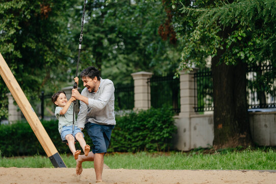 Happy father pushing son sitting on zip line in playground