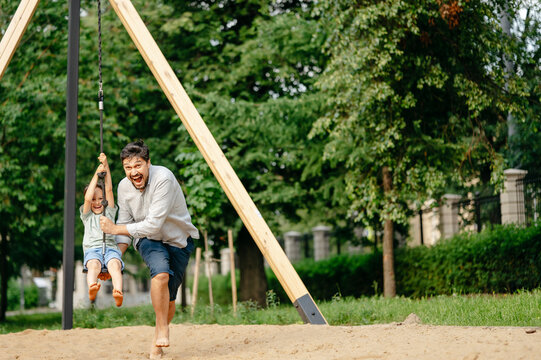 Carefree father pushing son sitting on zip line in playground