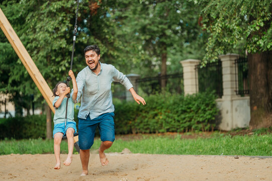 Cheerful father pushing son sitting on zip line in playground