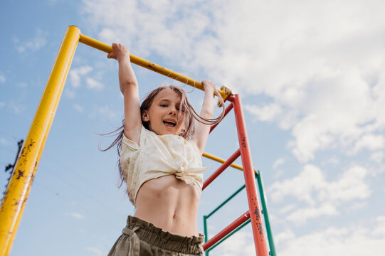 Playful girl hanging on monkey bar under cloudy sky