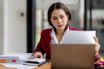 Serious and focused financial accounting on documents paper work at office, Asian woman use calculator and laptop for calculating reports and summarizing accounts, business at work in casual clothes.