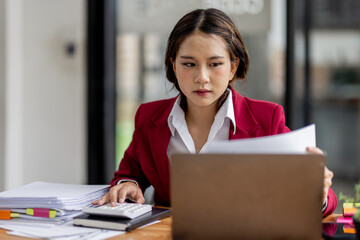 Serious and focused financial accounting on documents paper work at office, Asian woman use calculator and laptop for calculating reports and summarizing accounts, business at work in casual clothes.