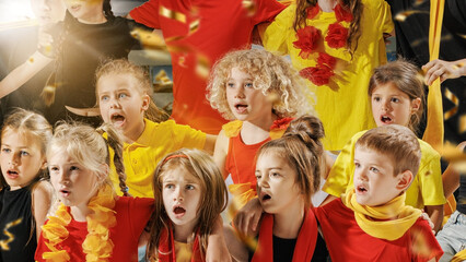 Group of children dressed in vibrant red, yellow, and black outfits spellbound watching their favorite team play on field, and golden confetti falling around them. Concept of young, sport, match. Ad