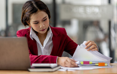 Serious and focused financial accounting on documents paper work at office, Asian woman use calculator and laptop for calculating reports and summarizing accounts, business at work in casual clothes.