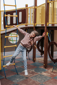 Happy girl hanging on rope ladder at playground
