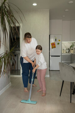 Mother teaching daughter to mop floor at home