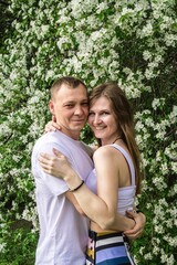 Fototapeta premium Happy couple in love hugging in a spring blossom garden with white flowers on the trees.