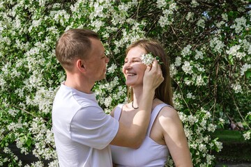 Young Couple in Love Hugging in Spring Garden with White Blossoming Trees on Floral Background.