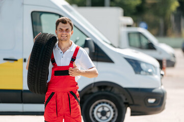 Young smiling man, in red coverall,  car mechanic holding auto tires