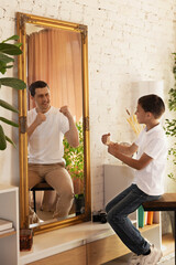 Boy and his adult version reflected in mirror, both mimicking playful fighting stance, shows joy...