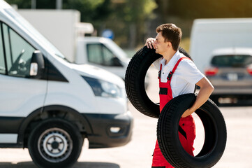 Young smiling man, in red coverall,  car mechanic holding auto tires