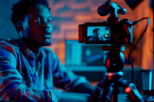 A young man records a vlog using a professional camera in a modern studio with vibrant lighting. Perfect for content creation, technology, and social media concepts