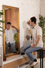 Man sits in front of mirror, adjusting hair, while his reflection shows younger version of himself...