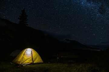 A mesmerizing view of a starry night sky with a glowing tent set up in the wilderness. The scene captures the peacefulness and beauty of camping under the stars, perfect for adventurers and stargazer