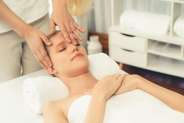 Fototapeta premium Caucasian woman enjoying relaxing anti-stress head massage and pampering facial beauty skin recreation leisure in dayspa modern light ambient at luxury resort or hotel spa salon. Quiescent