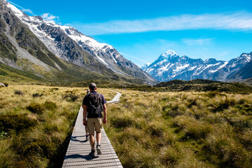 A group of hikers traverses a trail in Hooker Valley, surrounded by snow-capped mountains and vast...