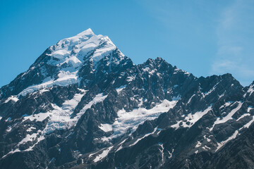 A close-up view of the snow-capped peak of Mount Cook, showcasing its rugged and majestic features. The pristine snow and clear blue sky highlight the beauty and grandeur of this iconic mountain in H