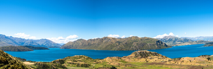 A panoramic view of a stunning mountain and lake landscape, showcasing the vastness and natural beauty of the region. The clear sky and calm lake create a peaceful and inviting atmosphere.