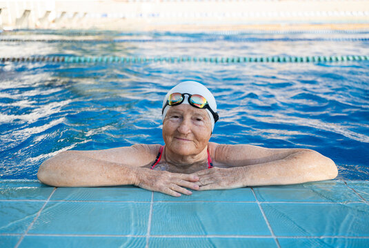 Smiling senior woman in swimming cap and googles resting on edge of pool