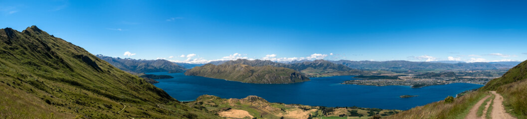 A panoramic view of a mountain and lake landscape, highlighting the vastness and beauty of the natural environment. The clear blue sky and expansive scenery create a tranquil and inviting atmosphere.