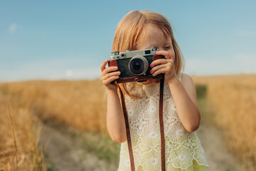 Blond hair girl taking photo with camera in wheat field