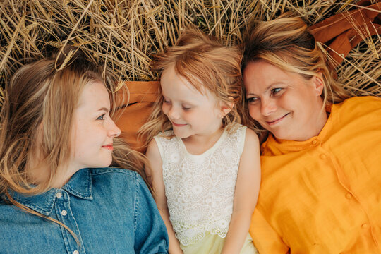 Smiling girl with mother and sister lying down on brown cloth over dry grass