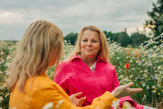 Smiling woman talking to sister sitting in chamomile field
