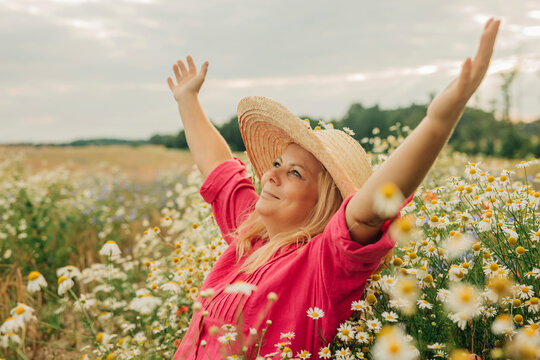 Happy woman wearing hat and sitting with arms raised at chamomile field